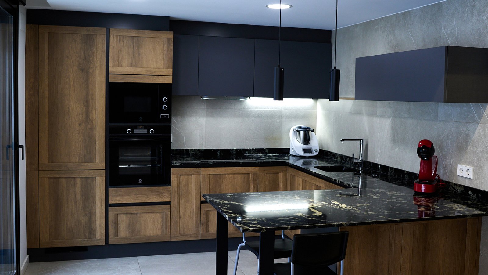 Reforma en cocina, azulejos grises y negros, granito negro en encimera. Electrodomésticos color negro.